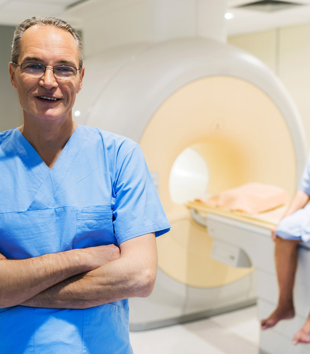Mature-male-radiologist-looking-at-the-camera-with-the-patient-in-the-background-before-calypso-fiducial-seed-placement-procedure